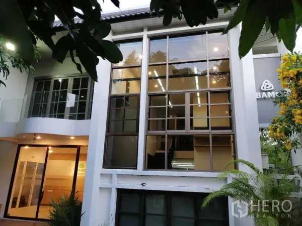 Home Office for rent in Watthana, Bangkok - Modern exterior facade featuring tall windows framed by trees.