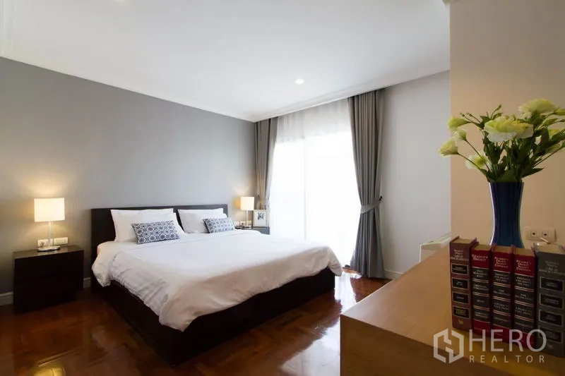 Condominium for rent in Watthana, Bangkok - Primary bedroom with king bed, soft gray accent wall, bedside lamps and sheer curtains.