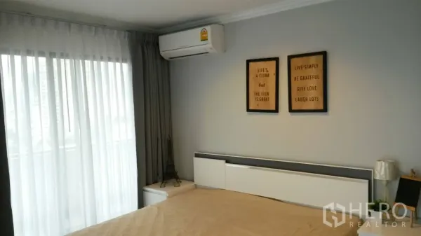 คอนโด ให้เช่าหรือขายในWatthana, Bangkok - มุมห้องนอนติดเครื่องปรับอากาศ หัวเตียง และกรอบรูปข้างผ้าม่านโปร่ง