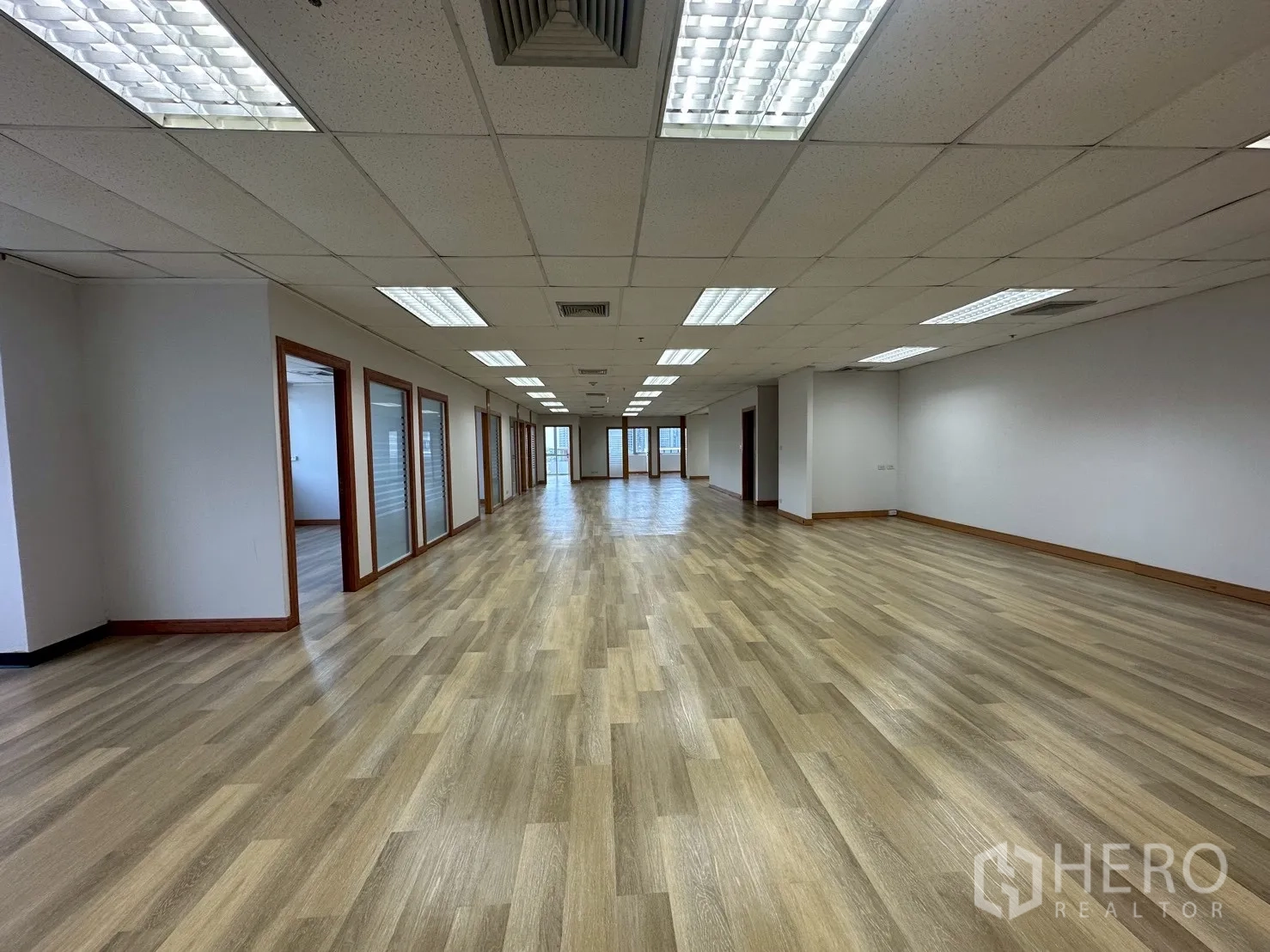 Office Space for rent - Open-plan office floor with rows of private glass-partitioned rooms and bright ceiling lights.