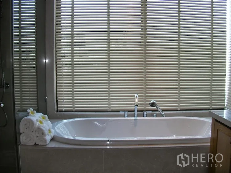 Condominium for rent in Khlong Toei, Bangkok - Bathtub by windows with blinds beside a double-sink vanity.