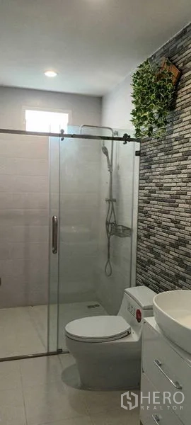Townhouse for rent or sale in Saphan Sung, Bangkok - Bathroom featuring glass-enclosed shower, stone accent wall and toilet.