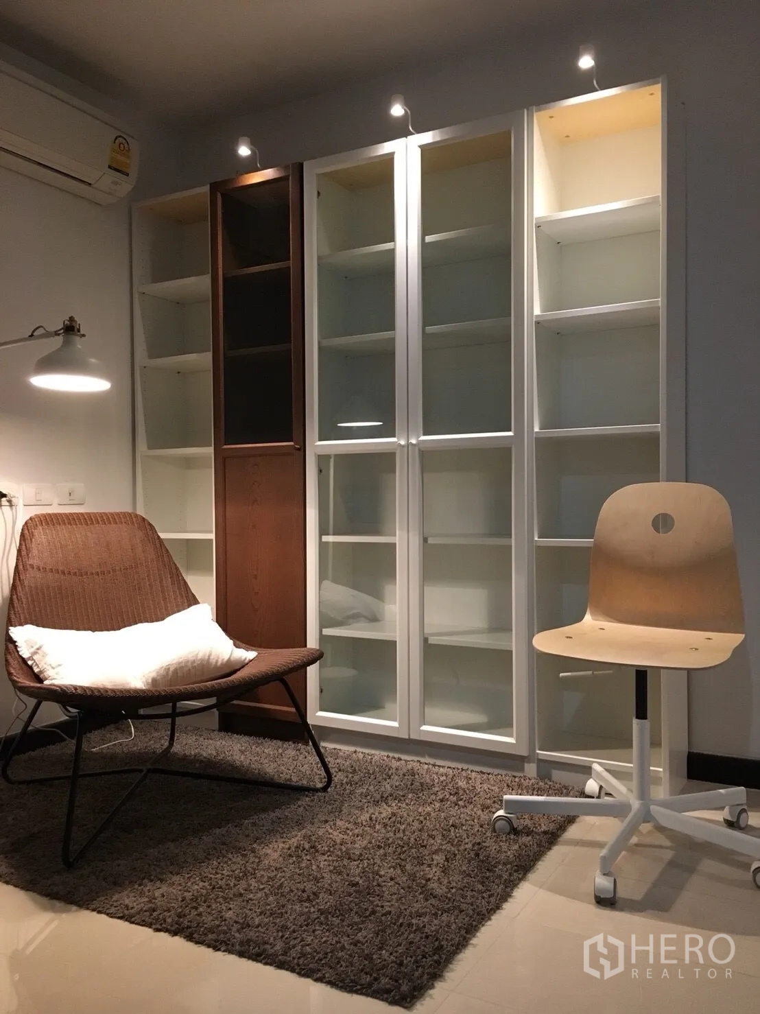 公寓 出租在Watthana, Bangkok - 温馨阅读角：藤编躺椅、地毯与带玻璃门的高柜，射灯照明。