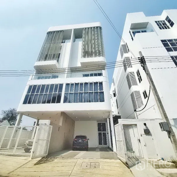 带办公室的家 出租或出售在Prawet, Bangkok - 曼谷Prawet现代白色五层Home Office外立面，竖向遮阳与电动大门车道。