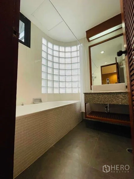 Condominium for rent - Bathroom with bathtub and curved glass-block wall beside vanity.