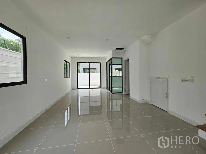 Townhouse for rent in Bang Kapi, Bangkok - Open-plan ground floor living and dining area with glossy tile floors, sliding glass doors and a glass-enclosed kitchen zone.