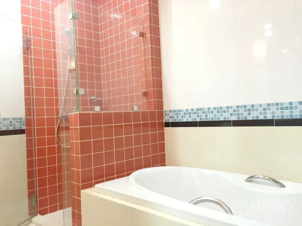 Condominium for rent in Khlong Toei, Bangkok - Bathroom with white bathtub and glass shower accented by orange mosaic tiles.