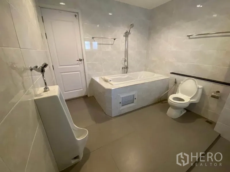 Townhouse for rent in Bang Na, Bangkok - Large bathroom featuring bathtub, toilet, wall urinal, and tiled walls.