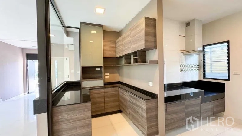 Detached House for sale in Bang Kapi, Bangkok - Modern L-shaped kitchen with wood cabinets and sleek black stone countertops.