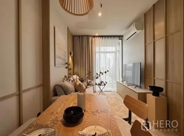 Condominium for rent or sale in Watthana, Bangkok - Warm modern living–dining room with wooden table, sofa, TV console, air conditioner and sheer curtains opening to a bright balcony.