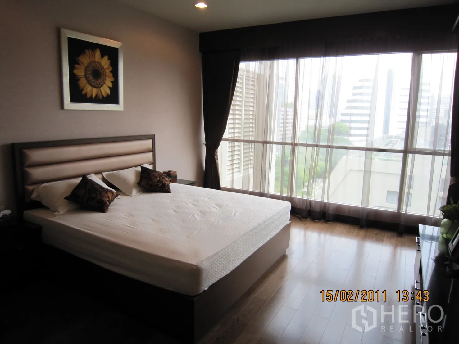Condominium for rent or sale in Pathum Wan, Bangkok - Bright bedroom with king bed, floor‑to‑ceiling windows, sheer drapes, hardwood floor, and city view.