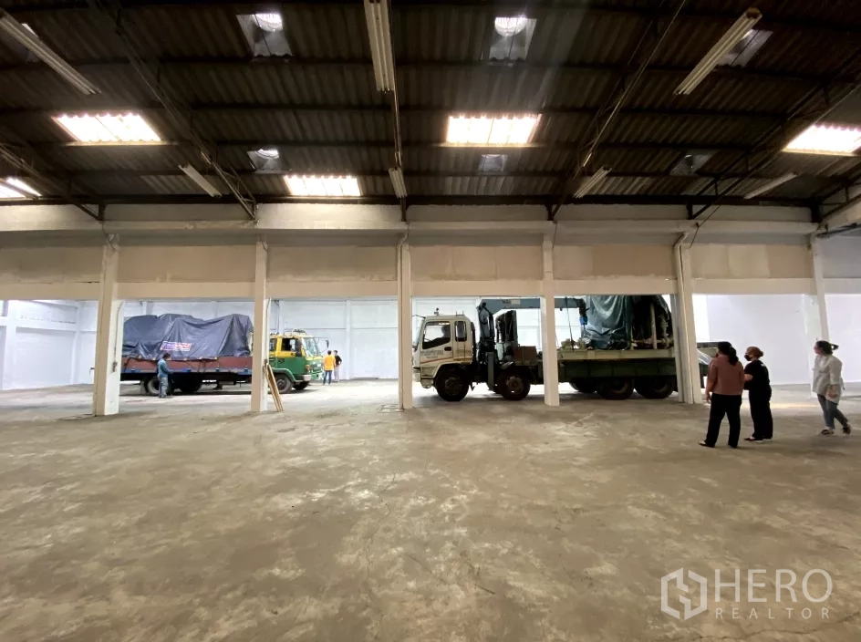 Factory for rent in Bang Phli, Samut Prakan - Expansive factory floor with a high steel roof, skylights and trucks along the loading area.