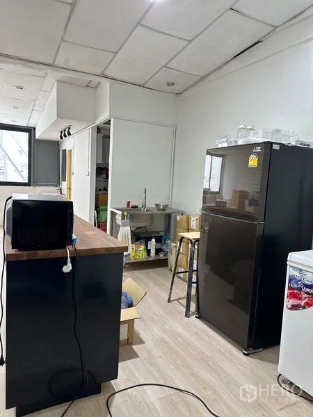 Shophouse for rent in Khlong Toei, Bangkok - Kitchenette view with fridge, microwave, open shelving and a stainless-steel sink.