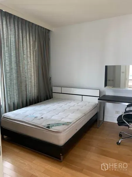 Condominium for rent in Khlong Toei, Bangkok - Bedroom with wood flooring, work desk and large window with blackout curtains.