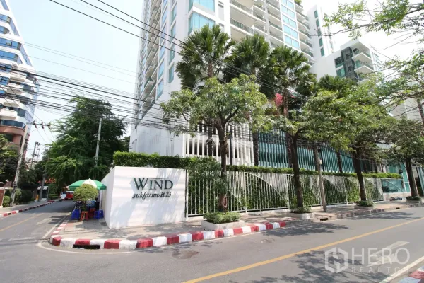 คอนโด ให้เช่าหรือขายในWatthana, Bangkok - ด้านหน้าอาคารคอนโดสมัยใหม่พร้อมรั้วและต้นปาล์มริมถนนเงียบสงบ