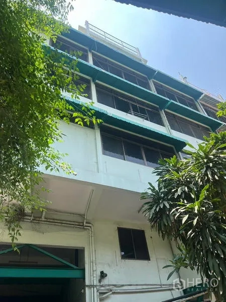 Warehouse for rent in Bang Kho Laem, Bangkok - Multi-storey warehouse-office facade with green awnings and trees.