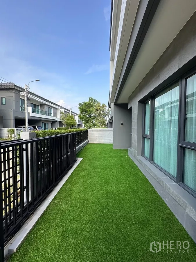 独立式住宅 出租在Bang Phli, Samut Prakan - 前侧草坪与黑色金属栏杆，临近大窗。