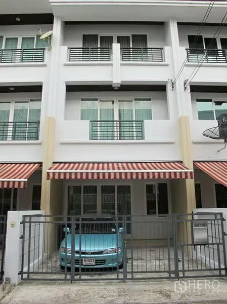 联排别墅 出租或出售在Wang Thonglang, Bangkok - 三层现代联排别墅外立面，带栅栏车位与条纹遮阳篷。