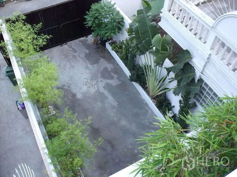 联排别墅 出售在Phra Khanong, Bangkok - 带大门的庭院车位，混凝土地面，两侧种有热带绿植