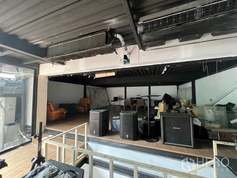 พื้นที่ขายปลีก ให้เช่า - ชานยกระดับสไตล์อินดัสเทรียลในร้าน มีลำโพง เก้าอี้หนัง และผนังกระจกด้านข้าง