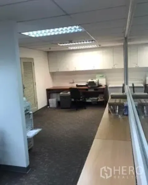Office Space for rent in Khlong Toei, Bangkok - Print and pantry zone with built-in white cabinets, desk and carpet flooring beside a glass partition.