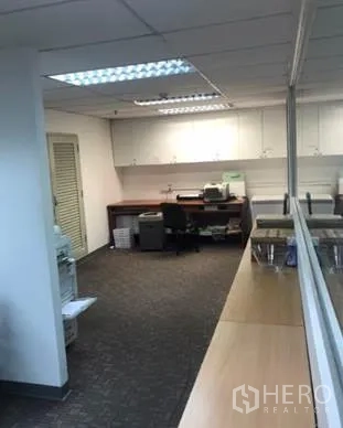 Office Space for rent in Khlong Toei, Bangkok - Print and pantry zone with built-in white cabinets, desk and carpet flooring beside a glass partition.