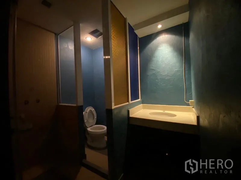 Retail Space for rent in Watthana, Bangkok - Restroom with blue walls, toilet cubicle, and vanity counter under spotlights.