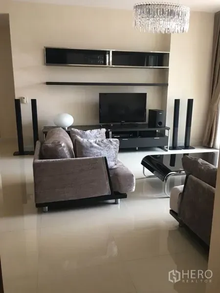 Condominium for rent in Bang Rak, Bangkok - Modern living room with grey sofas, glass coffee table, TV console, and crystal chandelier.