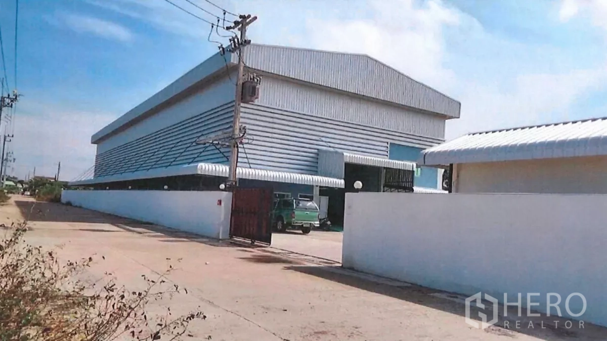 Factory for sale in Lat Lum Kaeo, Pathum Thani - Side exterior of the metal-clad factory along the road with perimeter wall and entrance gate.