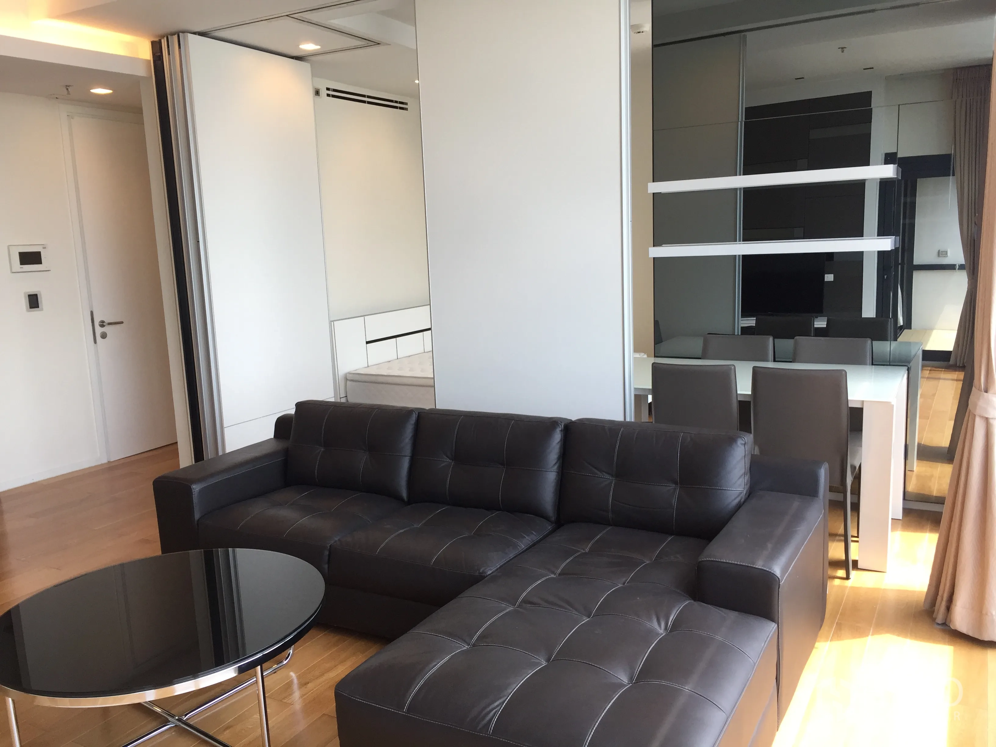 Condominium for rent in Ratchathewi, Bangkok - Leather sectional sofa facing a mirrored dining area in a bright contemporary interior.
