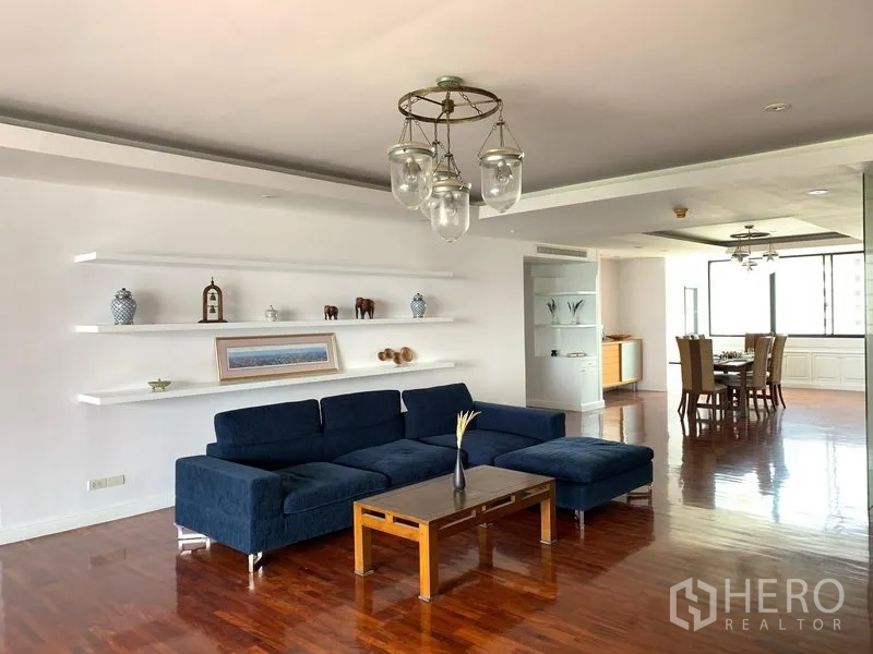 Condominium for sale in Khlong Toei, Bangkok - Bright open-plan living room with navy sectional sofa, white floating shelves and hardwood floors.