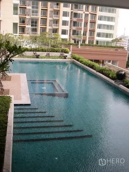 Condominium for rent in Sathon, Bangkok - Condominium swimming pool with submerged steps, landscaped greenery, and residential building backdrop.
