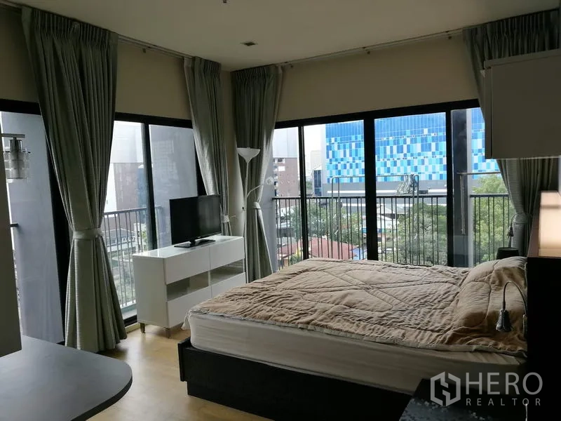 คอนโด ให้เช่าในWatthana, Bangkok - ห้องนอนมุมกระจกสูงจรดเพดาน มีระเบียง เห็นวิวเมือง เตียงคู่ ตู้วางทีวี และผ้าม่านสีเทา ในคอนโดเอกมัย