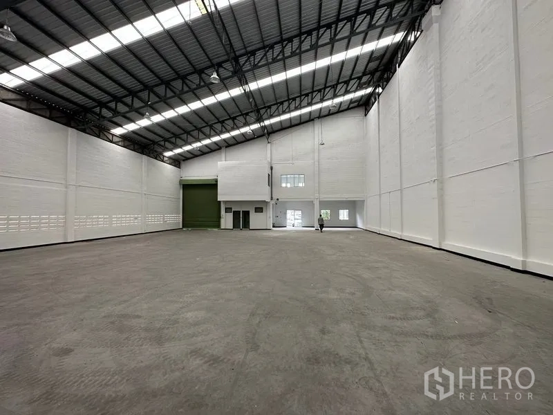 Factory for rent in Khlong Luang, Pathum Thani - Warehouse hall showing wide green loading shutter, mezzanine office block and polished concrete floor.