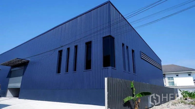 Warehouse for rent in Bueng Kum, Bangkok - Corner view of modern blue metal facade with vertical windows.