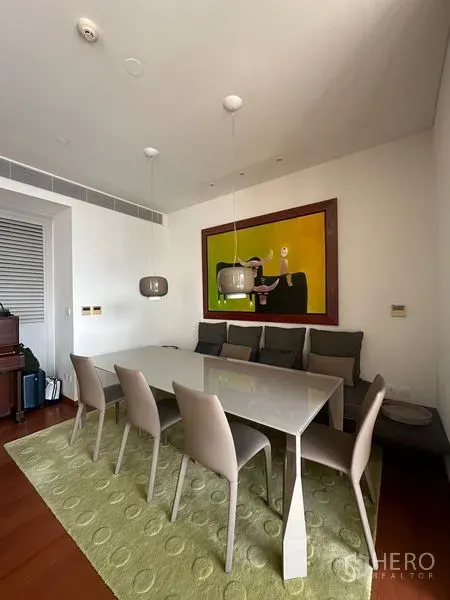 Condominium for rent or sale in Sathon, Bangkok - Bright dining area with a six-seat table, pendant lights, and large modern artwork on a green rug.