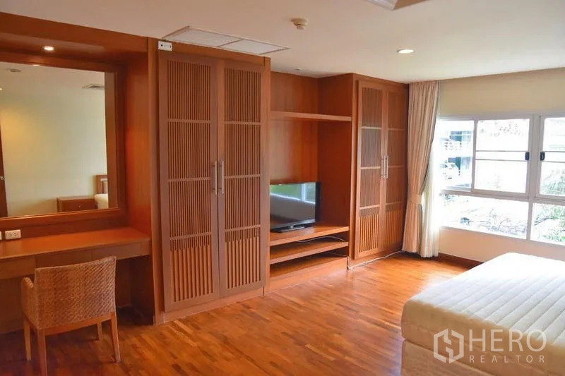 Apartment for rent in Sathon, Bangkok - Primary bedroom with wooden built‑in wardrobe, vanity and large windows.