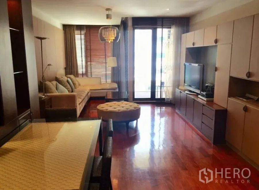 Condominium for rent in Pathum Wan, Bangkok - Open-plan living and dining room with wood floors, built-in media wall and balcony access.