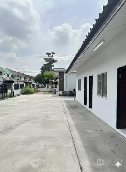 Home Office for rent in Bang Phli, Samut Prakan - Wide driveway and parking apron beside a white single-storey wing with doors and windows.