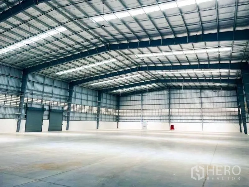 货栈 出租在Mueang Rayong, Rayong - 仓库内部带多扇卷闸门，挑高天花与采光天窗