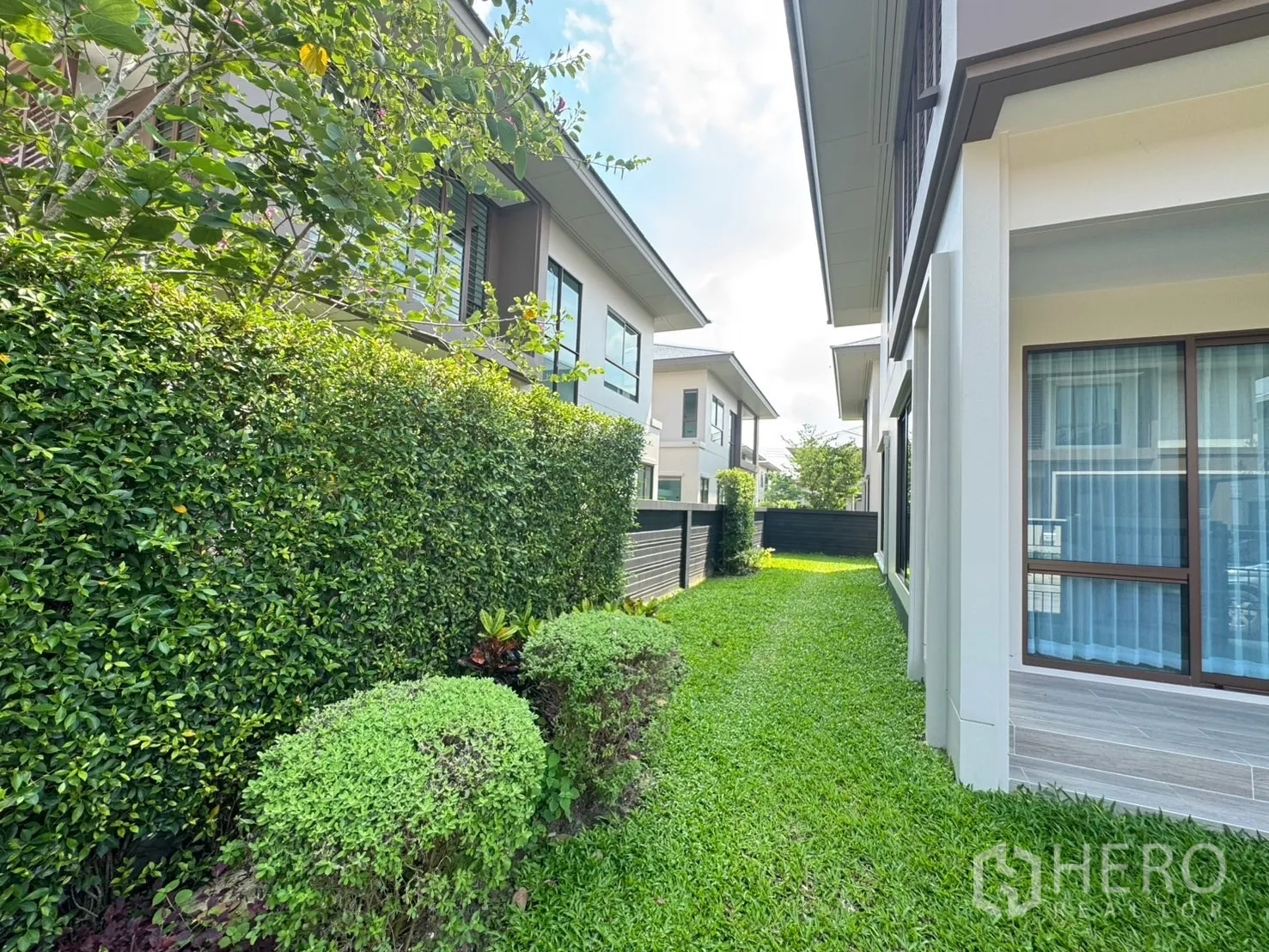 Detached House for rent or sale in Bang Kapi, Bangkok - Side garden with trimmed hedges and green lawn between neighboring houses.