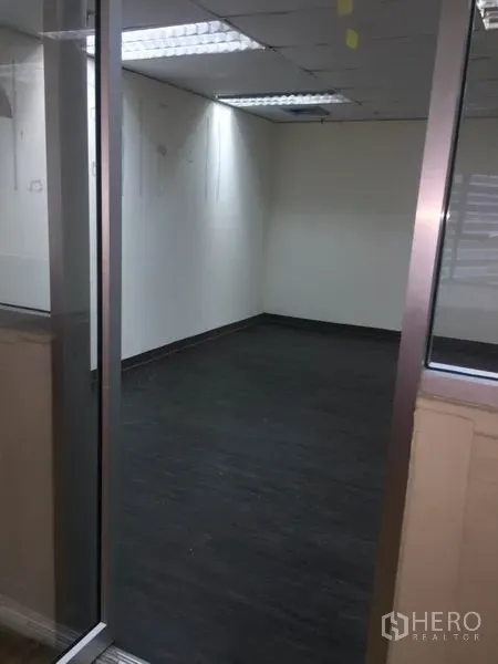 办公空间 出租在Watthana, Bangkok - 玻璃隔断的空置办公室，深色地板、白墙和嵌入式日光灯天花。