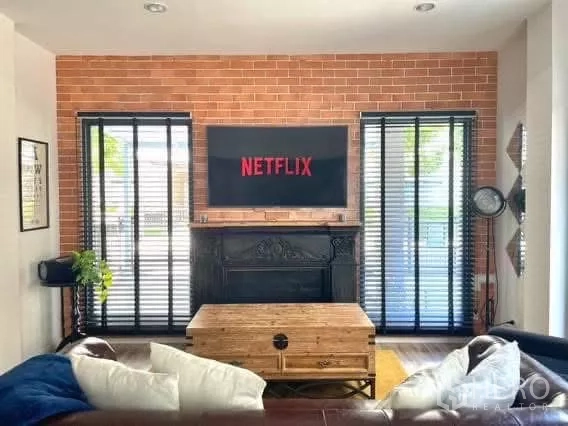 Detached House for rent in Saphan Sung, Bangkok - Living room with exposed brick feature wall, TV and tall windows with blinds.
