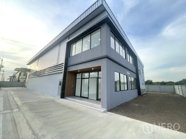 Factory for rent or sale in Bang Yai, Nonthaburi - Front corner of the building with glass entry, driveway and side yard.