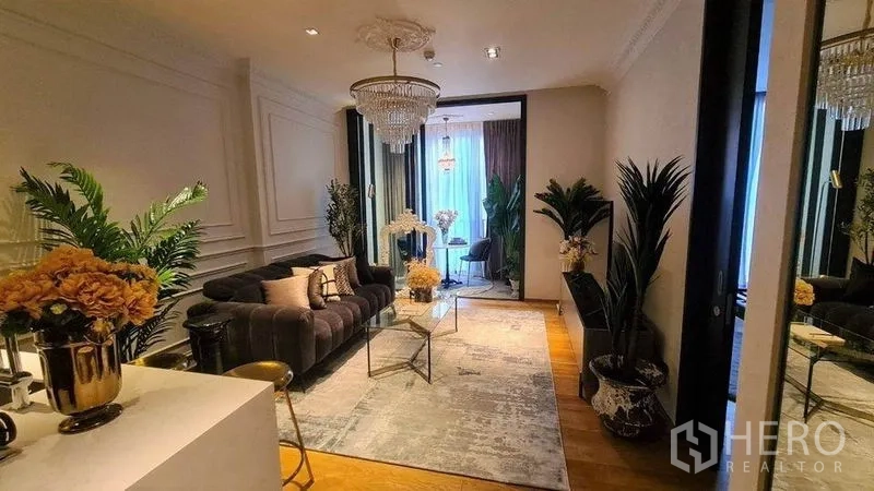 Condominium for rent in Khlong Toei, Bangkok - Open-plan living room with warm wood floors, chandelier and balcony-style nook.