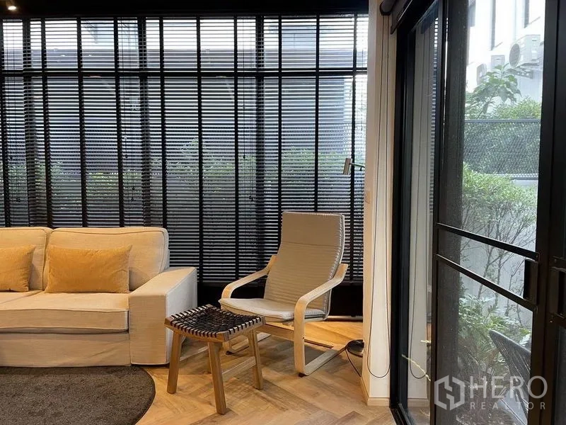 Detached House for sale in Sai Mai, Bangkok - Cozy living corner with sofa, lounge chair and floor-to-ceiling black blinds.