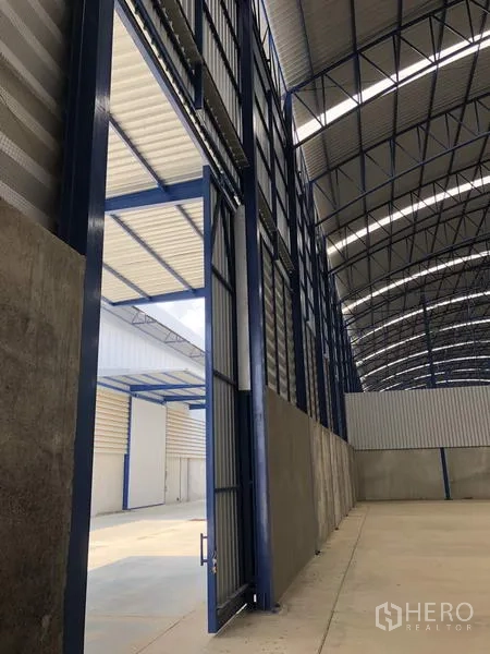 Factory for rent in Lat Lum Kaeo, Pathum Thani - Tall sliding industrial door and steel structure opening to an exterior loading area.