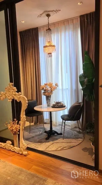 Condominium for rent in Khlong Toei, Bangkok - Small dining corner with two chairs, round table and chandelier framed by full‑height curtains.