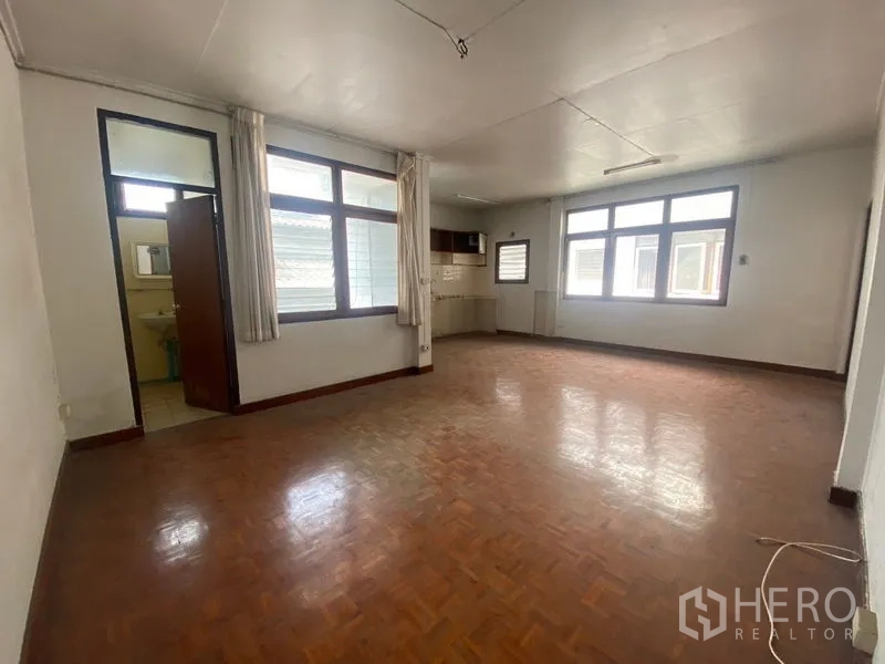 Home Office for rent in Khlong Toei, Bangkok - Spacious office room with parquet flooring, large windows, and a small kitchenette.