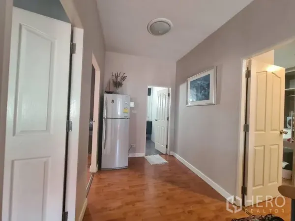 Detached House for rent in Sai Mai, Bangkok - Hallway with wood floors, white doors and a refrigerator connecting multiple rooms.